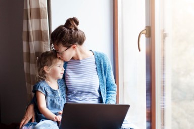 Mother and young daughter sat at window seat on laptop